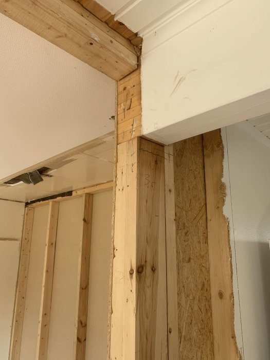 Hörn i ett rum under konstruktion där en regel har avlägsnats från en limträbalk, exponerande spikar och OSB-skivor.