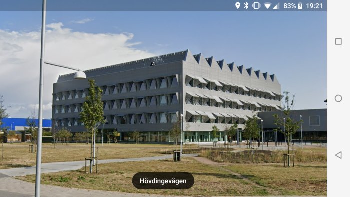 Modernt byggnad med ovanlig geometrisk fasad, sett på dagtid från en park.