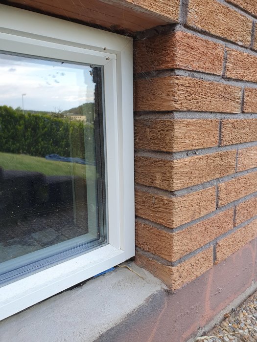 Närbild på nyinstallerat aluminiumfönster med putsad leca ovanför och tegelsten runt sidorna.