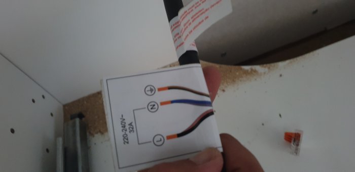 En hand som håller en installationsinstruktion för en induktionshäll, med Wago-klämma synlig.