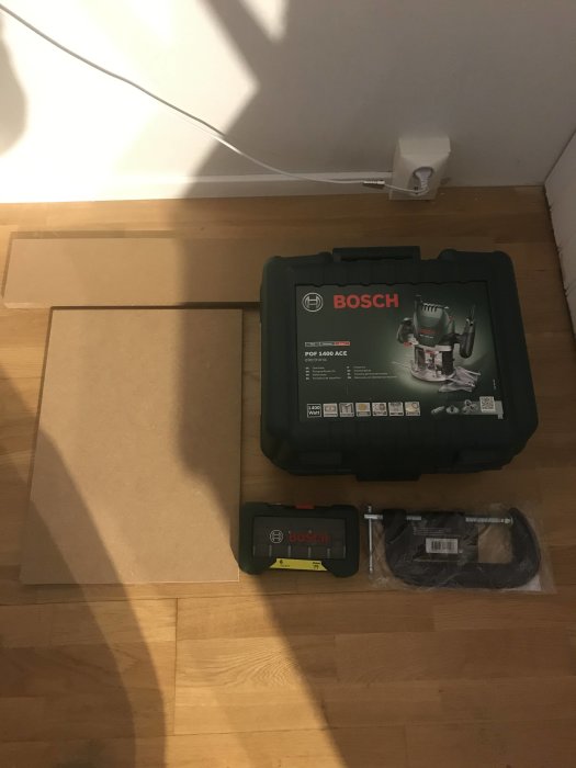 Bosch-fräs i låda med tillbehör på trägolv redo för träarbeten.