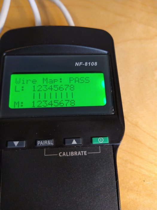 Kabeltestare som visar "Wire Map: PASS" på skärm med grön bakgrund och anslutna kablar i bakgrunden.