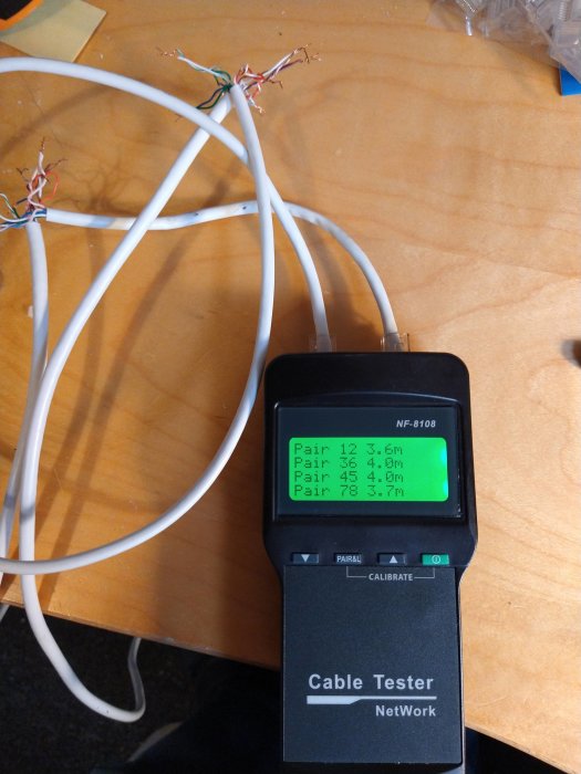 Kabeltester som visar resultat på skärm med flera ethernetkablar i bakgrunden.