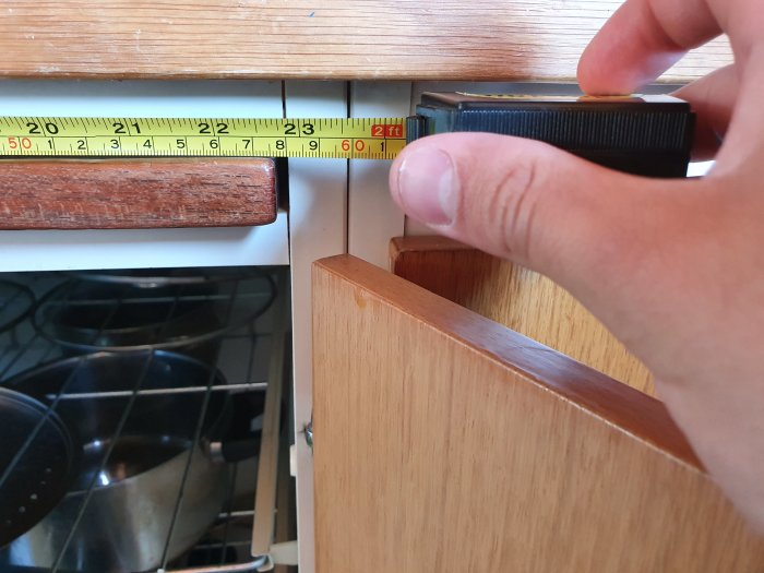 Hand håller måttband vid köksskåp och mätspace mellan skåp och spis för diskmaskinsinstallation.