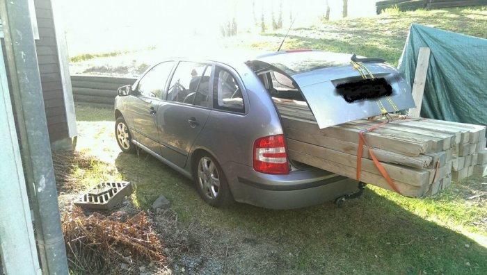 Bil lastad med plankor och takplåt säkrade med spännband, uppställd utomhus.