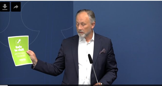 Man på presskonferens presenterar anslag med texten "Safe to visit".