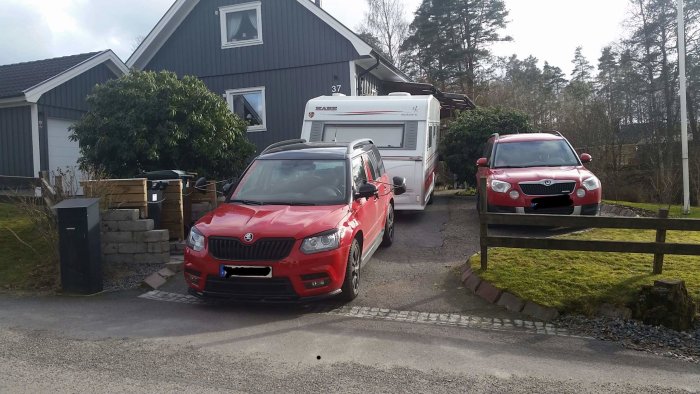 En röd bil backar in framför ett hus medan en husvagn parkerats på uppfarten och en annan bil står vid sidan.