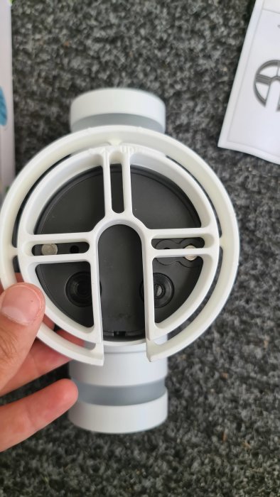 Hand håller en grå och vit Ecolite Lyra utomhuslampa med synliga distansklossar mot en mörk bakgrund.