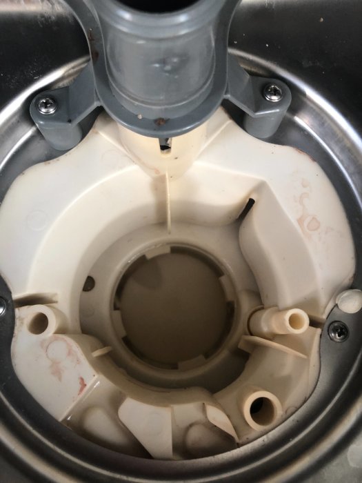 Inre delen av en diskmaskin där en vit plastbit är felplacerad nära pumpen.