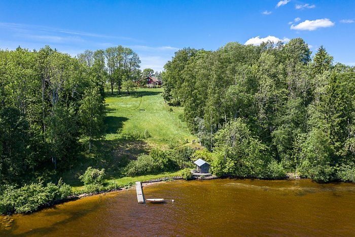 Flygbild över sjön Fryken med brygga, båt och hus omgivet av grönska i Värmland.