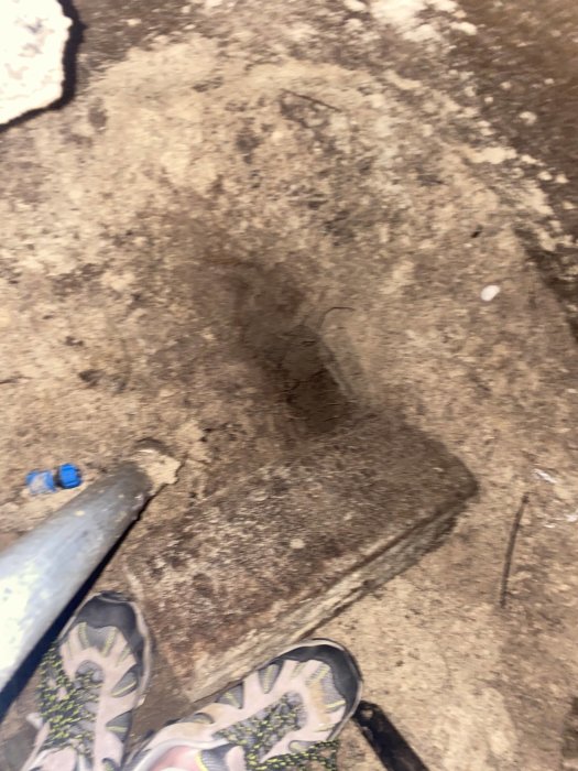 Botten av ett grävt hål med en spade och skor som ger perspektiv på hålets djup och storlek.