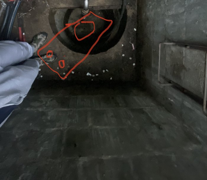 Personens ben vid ett hål i betonggolvet markerat för filterbrunn med en röd kontur, avsedd för installation av stupstock.