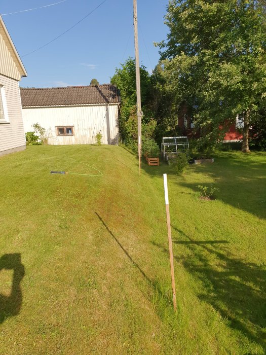 Gräsmatta med markerad höjdskillnad på ca 90 cm där en tidigare stödmur avlägsnats, intill en bostad.