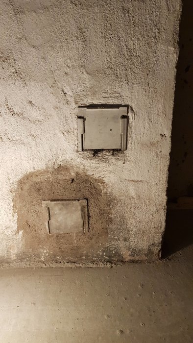 Murstock med gamla rensluckor och igenmurat hål i betongvägg, avsedd för byggnadsrenovering.