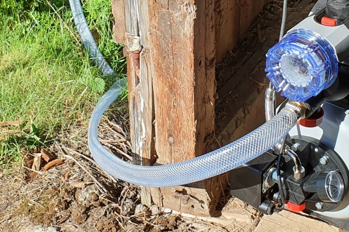 Transparent slang ansluten till en vattenpump med sughöjdsproblem, nära en trädstruktur.