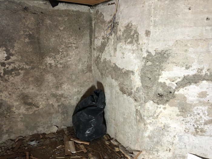 Rå betonghörn av ett rum med skräp och svarta plastpåsar, ojämn yta inför renovering.