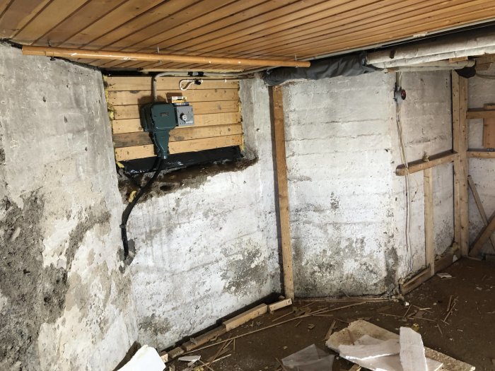 Omförvandlat rum med oputsade betongväggar, brutet tak och synlig elinstallation, avsett för förråd.