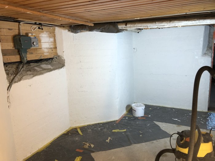 Renoveringsprojekt med nymålade vita källarväggar, en öppen färgburk och en dammsugare på golvet.