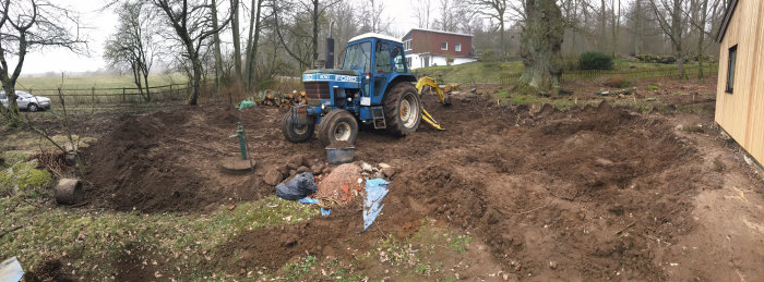 Panoramabild av en trädgård under uppgrävning med en blå Ford traktor och ojämn mark.