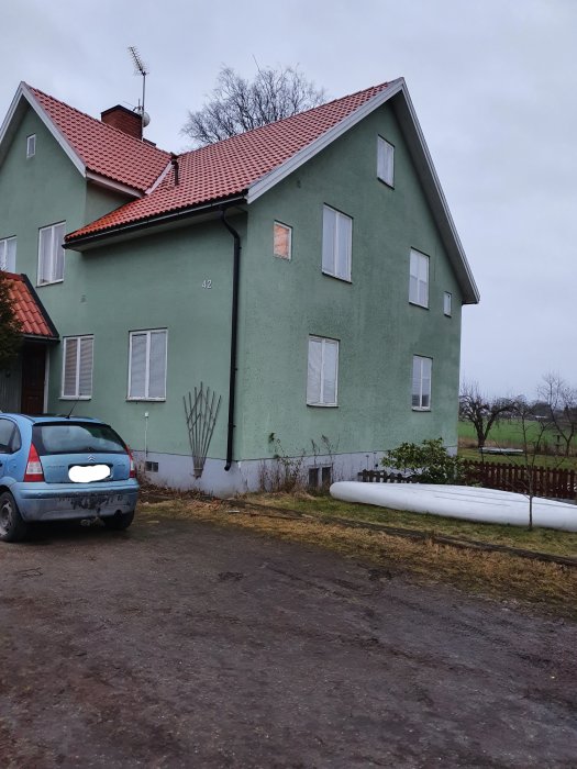 Tvåvåningshus med gröna väggar och rött tegeltak, grått framför huset och en bil på uppfarten.