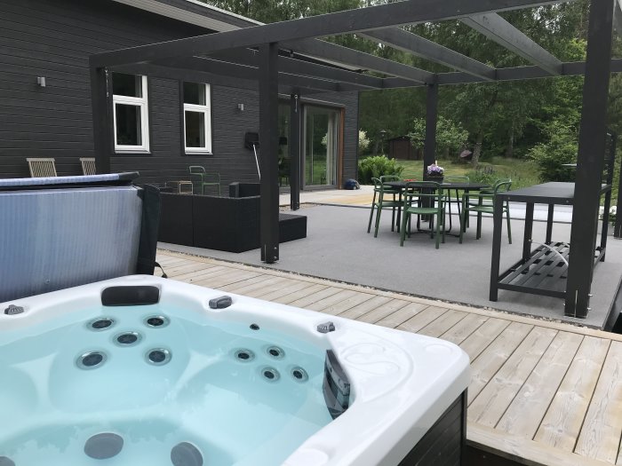 Uppvärmd jacuzzi på trädäck med uteplats och möbler i en trädgård.