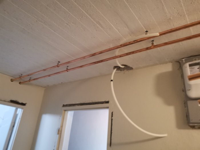 Kopparledningar i källartak med märkning inför kapning för installation.