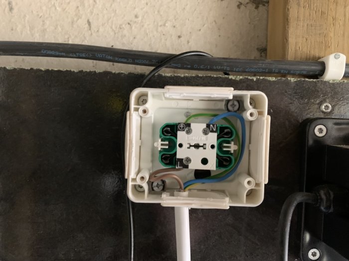 Elektriskt vägguttag utan frontplatta med öppen kabeldragning och anslutna kablar märkta N och J.