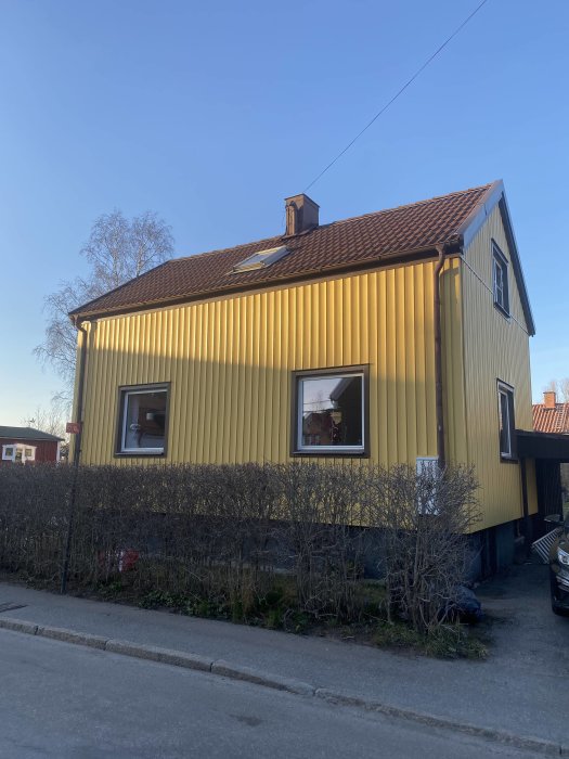 Ett gult hus med plåtfasad och nytt tak under renovering i ett bostadsområde.