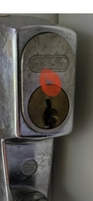 Närbild på en oöppnad ASSA-låscylinder med synlig borrmarkering.