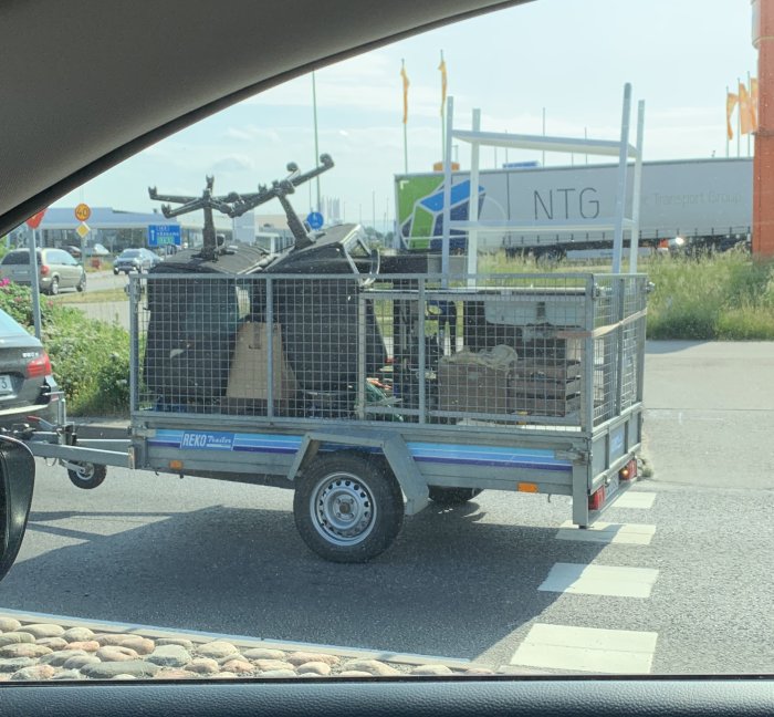 Lastsläp med byggmaterial och verktyg parkerat på en gata sett från en bil.