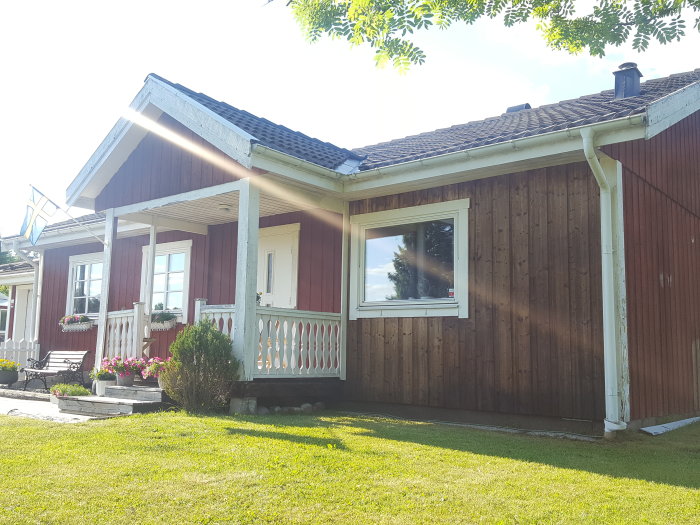 Delvis renoverad fasad av trähus, nytvättad vägg vid fönster med synlig gammal färg, blomlåda borttagen.