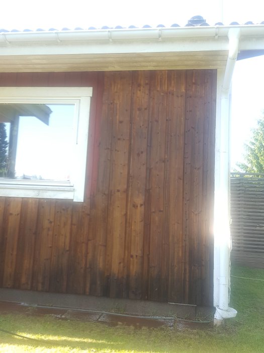 Delvis rengjord trävägg på husets framsida med synlig skillnad mellan ny och gammal färg vid fönstret.