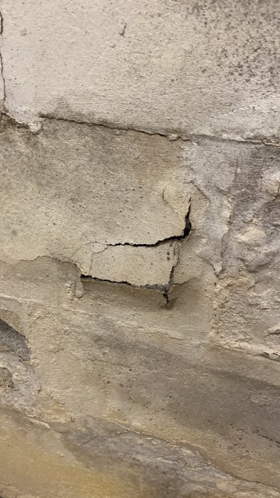 Fuktskadad lättbetongvägg med sprickor och flagande färg i källare.