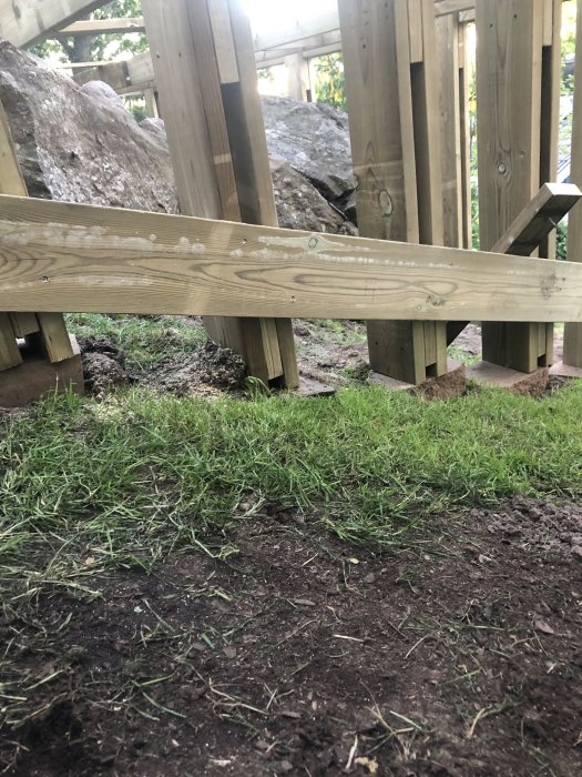 Nybyggd trätrappa i en trädgård visar steg och räcken med stora stenar och gräsmatta i bakgrunden.