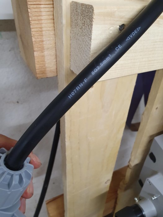 Anslutningskabel 5g2.5mm² hålls upp framför en pelarborrmaskin, text synlig på kabeln.