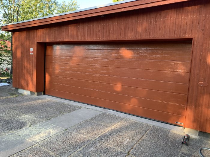 Nyinstallerade träpaneler på garage med brun garageport och detaljer som ska färdigställas.