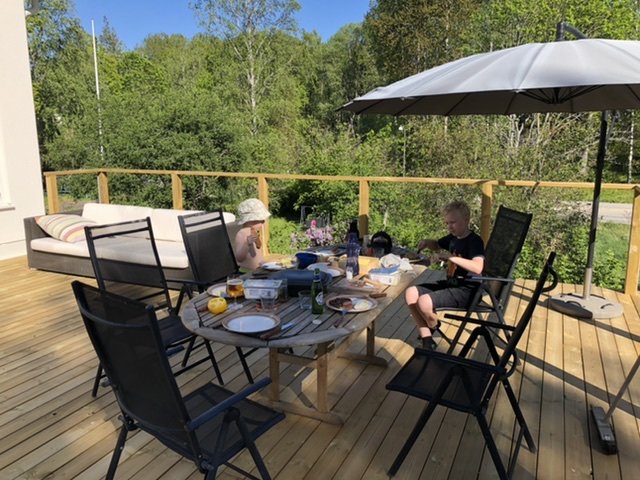 Nybyggd träaltan med räcke, möbler och familj som njuter av en måltid utomhus under ett parasoll.