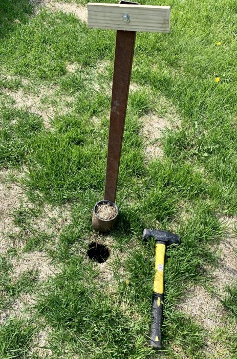 Manuell gräsmatteluftare och hammare på gräsmatta bredvid hål med borttagen jordplugg.