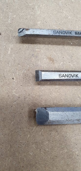 Tre stämjärn från Sandvik i varierande skick på en brun arbetsyta.