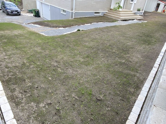 Nyanlagd gräsmatta med sparsam gräsbeväxt framför ett hus, bevattningssystem delvis synligt.
