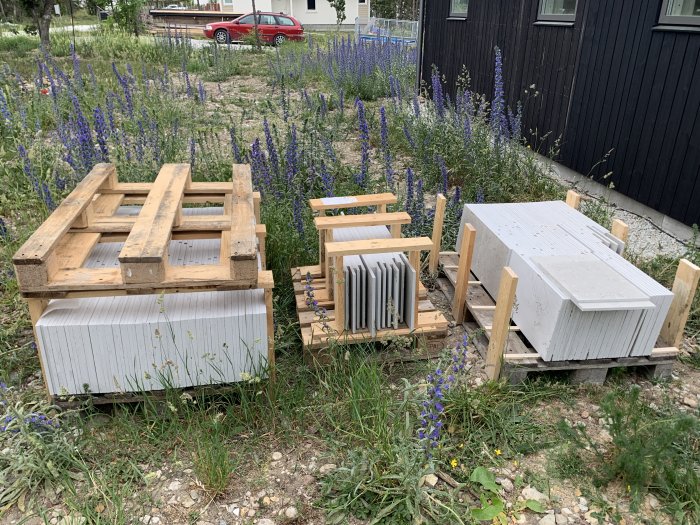 Kalkstensplattor på pallar redo för läggning omgivna av blå lupiner på en byggarbetsplats.