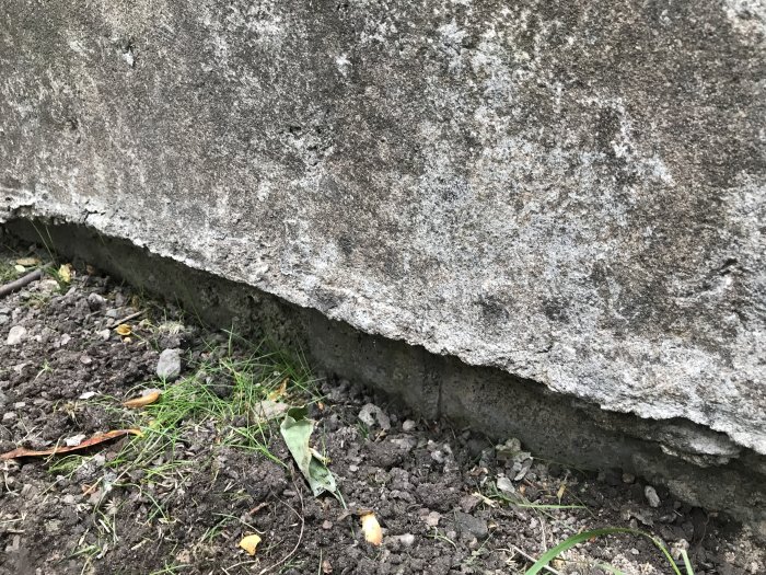 Sliten trappkant av betong intill en rabatt i behov av reparation och renovering.