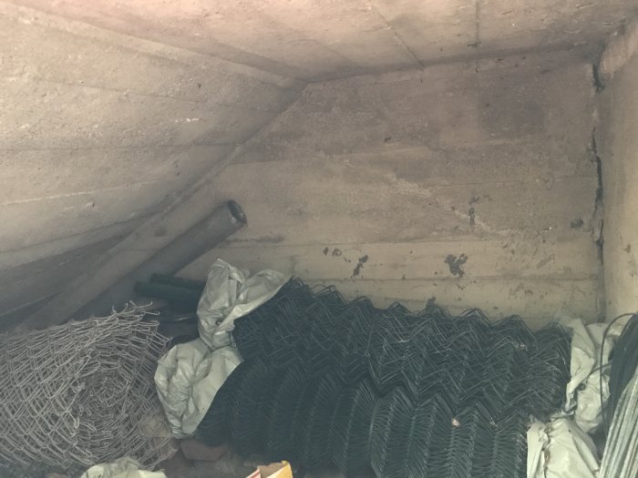 Utgånget betongtrappsteg med sprickor och högar av nät och rör lagrade under, behov av renovering.
