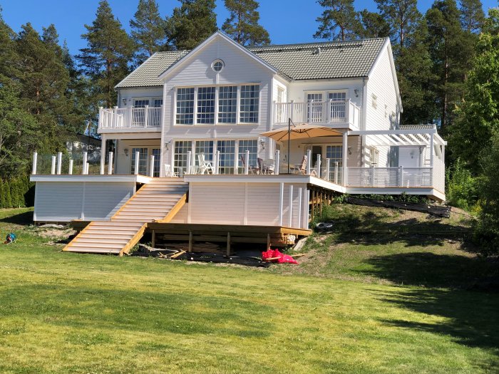 Renoverad vit villa med altan under konstruktion, pergola och gräsmatta i soligt väder.