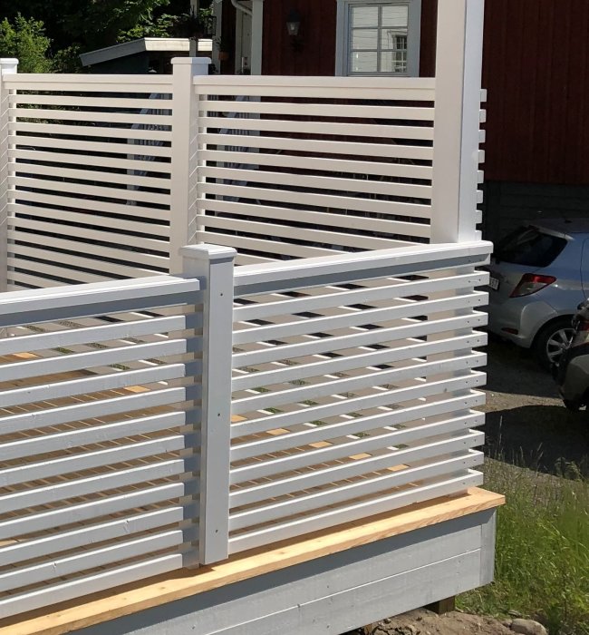 Vitmålad pergola med horisontella ribbor och en översta ribba som inte ligger dikt mot stolpen.