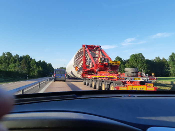 Lastbil med lång, ovanligt stor last märkt "Convoi Exceptionnel" på en landsväg sett från insidan av en bil.