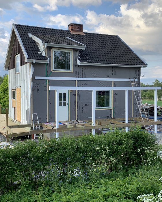 Hus under renovering med tillbyggnad av trädäck, vindskydd och isoleringsexponering.