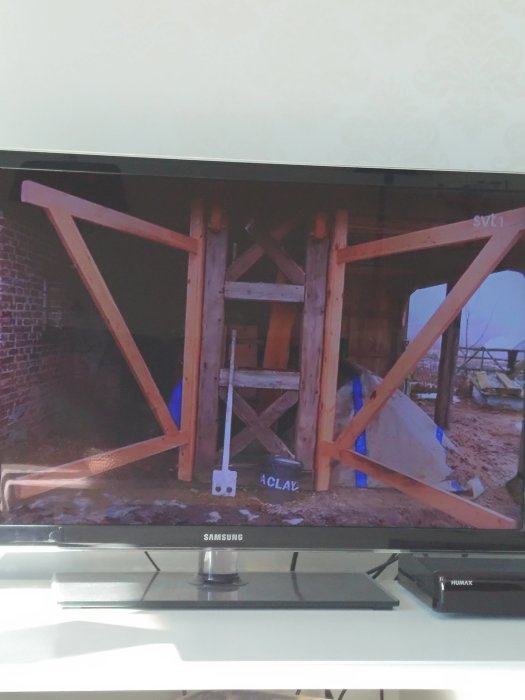 Tv-skärm som visar trästomme till byggprojekt med stödstolpar och korsande brädor.