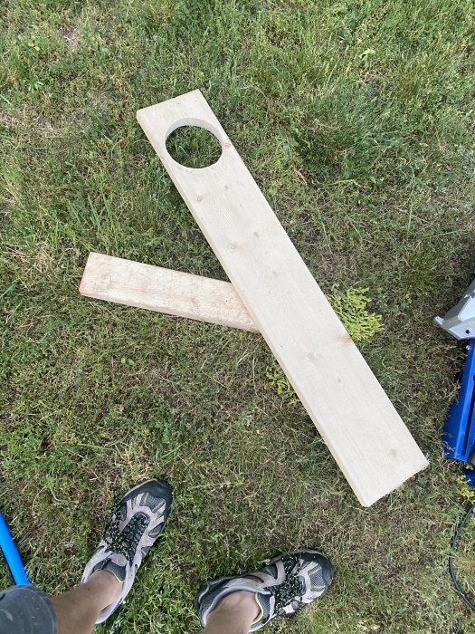 Person som står på gräsmatta med träplanka med utskuret hål och verktyg för brunnsbygge.