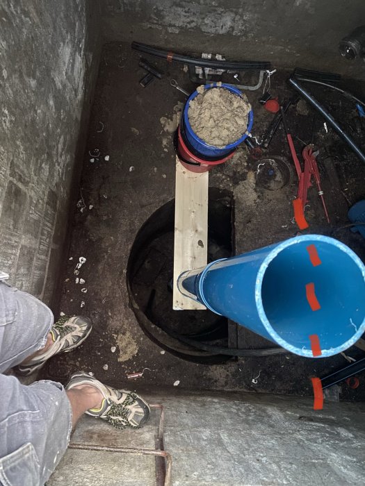 Vy inifrån en brunn under renovering med verktyg, ett borrat hål och en träplanka för stabilisering.
